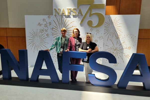 picture of three people standing next to big letters which read out "NAFSA" at the 75th NAFSA Conference